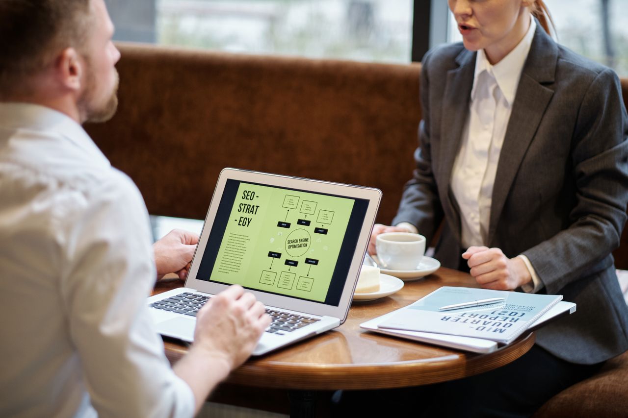 Un homme et une femme participent à une réunion professionnelle pour discuter d’une stratégie SEO dans l’ambiance chaleureuse d’un café.